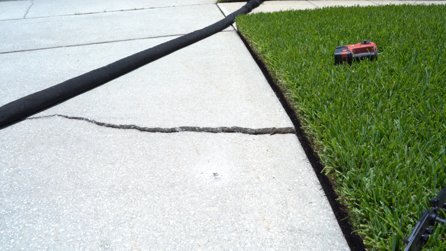 Cracked concrete on sidewalk of home next to grassy yard