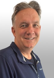 Smiling man with short hair wearing a navy zip-up jacket against a light gray background.