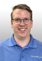 Smiling person wearing glasses and a blue polo shirt against a gray background.
