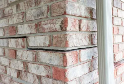 Brick wall with a visible crack and misaligned bricks, showing structural damage and possible need for foundation repair.