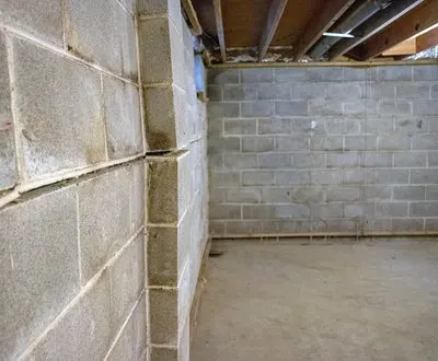 Cracked concrete block wall in basement, showing structural damage and misalignment, may require foundation repair.