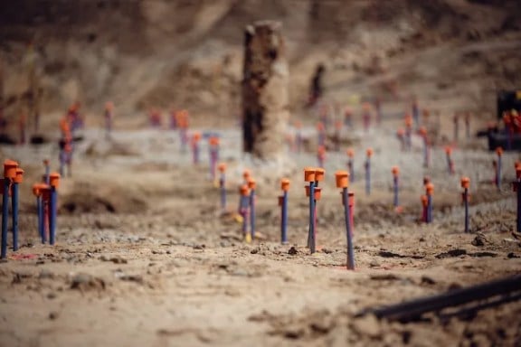 Numerous survey stakes with orange caps are placed in dry, rocky soil at a construction site.