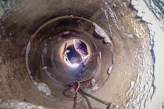 View from inside a narrow, rough pipe looking out at a person standing at the opening in daylight.