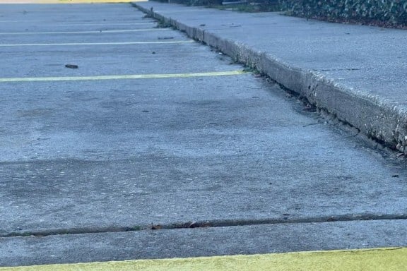 A sidewalk curb next to an empty parking lot with yellow painted lines.