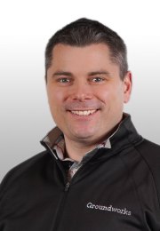 Smiling man in a black Groundworks jacket with a light gray background.