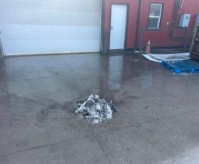 Small pile of dirty snow melting on a wet concrete surface near a red building with a garage door.