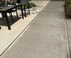 A patio table with potted flowers sits next to a slightly raised concrete sidewalk.